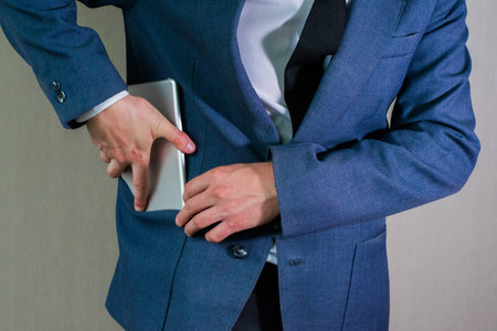 Young businessman in a white shirt hides a tablet in his jacket pocket