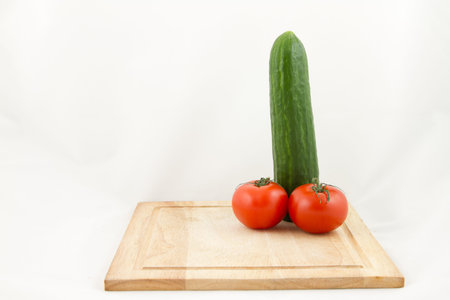 A wooden chopping with a phallic combination of cucumber and tomato isolated on white.の写真素材