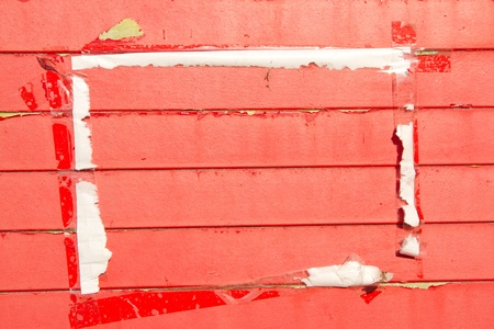 Wooden horizontal slats painted red with areas of flaking paint and a framed area with a paper and tape surround.の写真素材