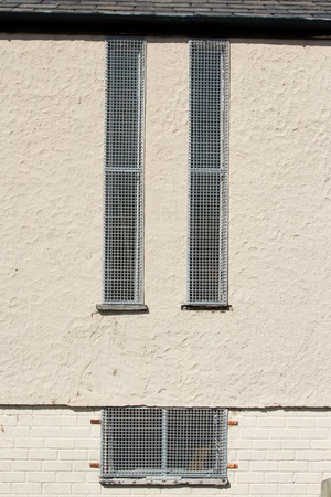 Metal security grills fixed to a wall covering windows to a building for crime prevention.の写真素材