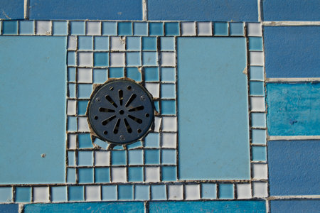 A round metal drain cap with screw fixings set into a blue and white ceramic tile pattern.の写真素材