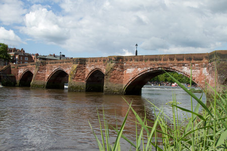 An historic red sandstone bridge with arches and a flowing river against a sky with cloud.の写真素材