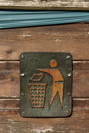 A metal litter sign screwed to a wooden bin showing a figure putting litter in a bin.の写真素材