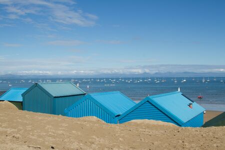Blue beach huts in the sand look out over the sea with yachts and mountains in the distance at Abersoch, Gwynedd, Wales, UK.の写真素材
