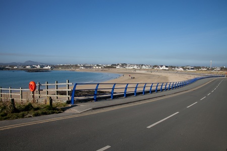 A path and railings curve around the sandy beach of Trearddur bay, Anglesey, Wales, UK.の写真素材