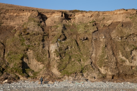 A man stands and looks up under a steep bank with areas of landslide errosion.の写真素材