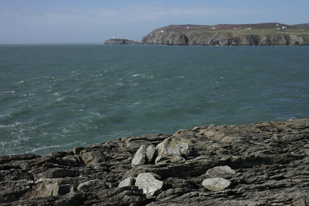 A view from rocks across a bay to south stack lighthouse in the distance, Wales coast path, Anglesey, Wales, uk.の写真素材