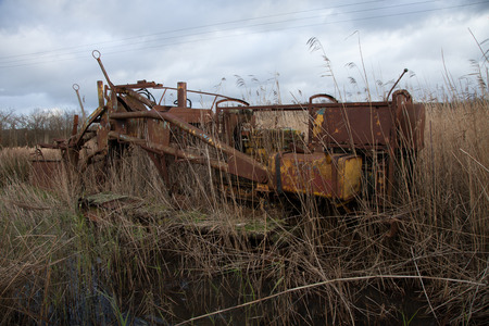 Cleared reeds reveal a tracked rusty vintage wetland machine complete with gearbox, fuel tank, hydrolics and a ditch water barrier in the distance.の写真素材