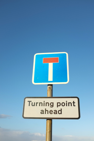 A dead end sign on a pole with a turning point sign underneath against a blue sky.の写真素材