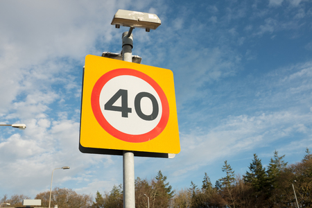 A road traffic sign with '40' in a red circle against a yellow background with a blue cloudy sky in the distance.の写真素材