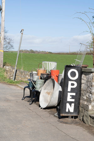 Open sign next to pots, tubs, buckets and bric-a-brac on the roadside outside a junk shop in the countrysideの写真素材
