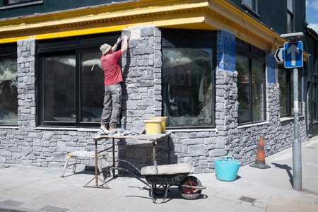 Construction worker on a trestle fixing stone facing to the outside of a building.の写真素材