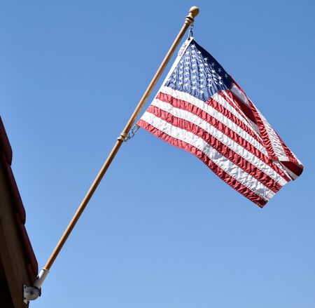 The U.S. flag waves in the wind as it is juxtaposed against a clear blue sky outside my house.の写真素材