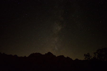 Amidst a sea of stars, the Milky Way galaxy shines high above dark hills and trees in a California desert.の写真素材