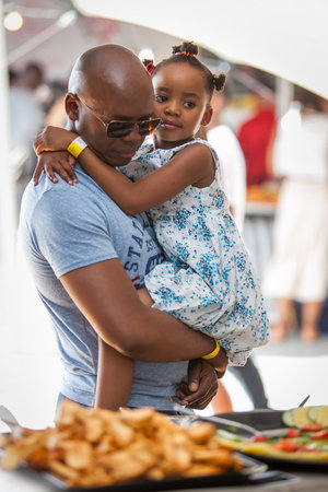 Johannesburg, South Africa - November 2, 2015.Man looking at food at event, with his daughter in his arms.のeditorial素材