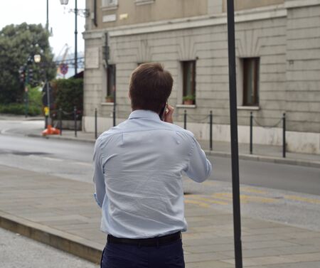 a young business man is calling someone while walking through the streetsの写真素材