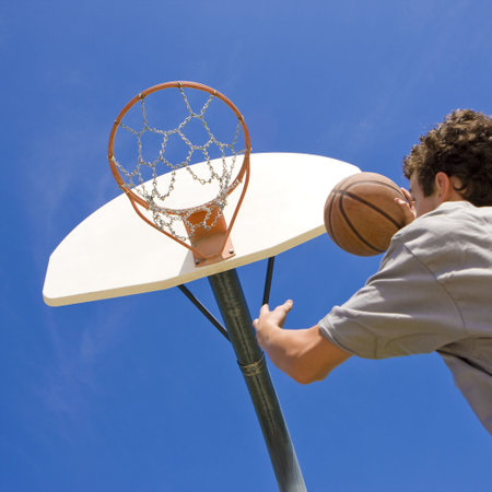 A teen basketball player jumps to shoot at the basket