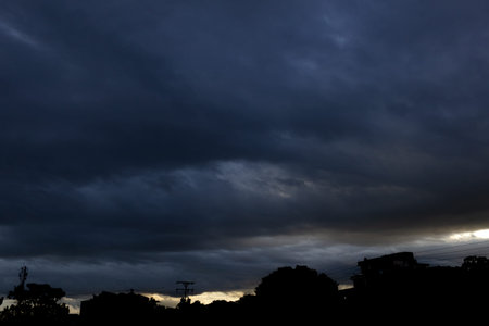 Dark clouds in the sky over the city. Silhouettes of houses and trees.