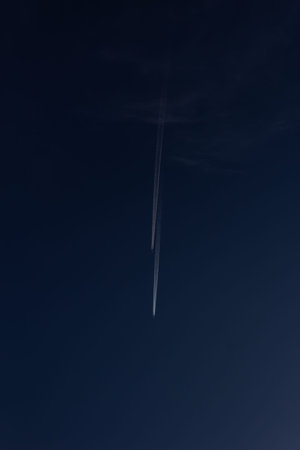 Airplane in the blue sky with a trail of contrail.