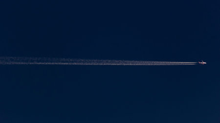 Airplane in the blue sky with contrails in the air.