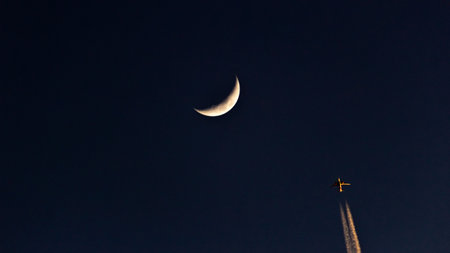 View of the plane and the crescent moon in the night skyの写真素材