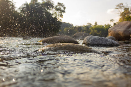 Rocks in the river with water splashing at sunset, Thailand.