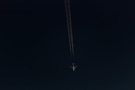 Airplane flying in the night sky with contrails of the planeの写真素材