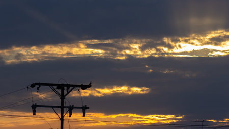 Silhouette of electric pole at sunset with clouds in the sky