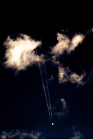 Airplane trail in the night sky with clouds. Toned.