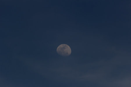 Moon in the dark blue sky with white clouds. The moon is the second half of the day.の写真素材