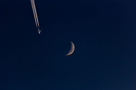 Moon and airplane in the night sky with contrail, view from below