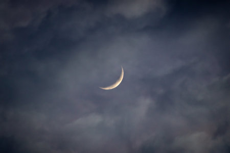 Crescent moon in the dark cloudy sky in the evening time.の写真素材