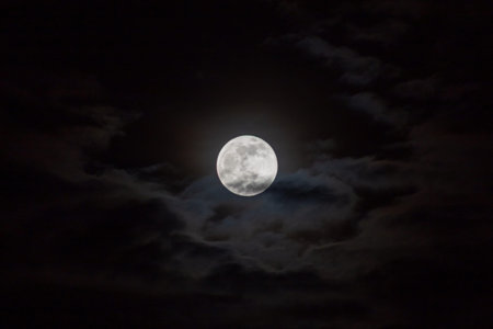 Full moon in the night sky with dark clouds. Natural background.