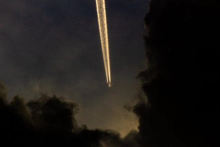 Airplane trail in the night sky with clouds in the background.