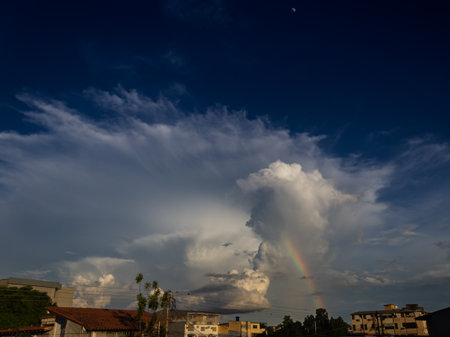 Rainbow in the blue sky with clouds and city in the backgroundの写真素材