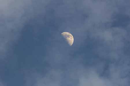 Moon in the blue sky with white clouds. Close-up.