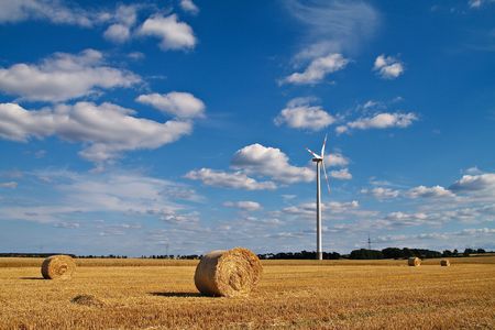 Bales of straw and a windmill on a field in the light of a sunny day.の写真素材