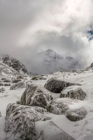 Stunning peak in the clouds and beautiful ice flowers on the rocks after a winter storm at the Rila mountain in Bulgaria, Maliovica.の写真素材
