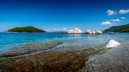 Sunny day over the rocky coast and a lonely island in the sea with beautiful azure water at the Skopelos island in Greece.の写真素材