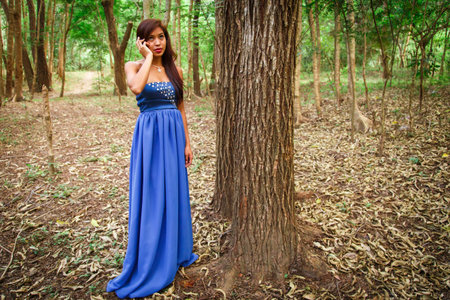 atractive latin woman using phone at forest with blue dressの写真素材