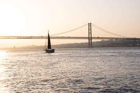Sailing boat sailing in front of a bridge during sunsetの写真素材