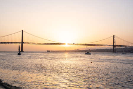 Sunset in a river with a bridge and a sailing boatの写真素材