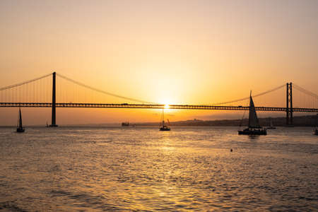 Vivid sky during sunset in a river with a bridge and a sailing boatの写真素材