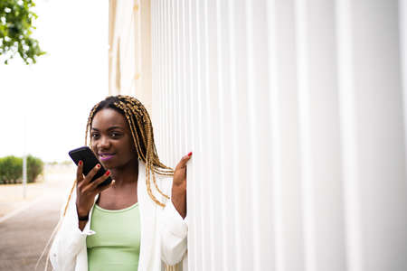 Portrait of an black woman sending a voice message with the mobile outdoorsの写真素材