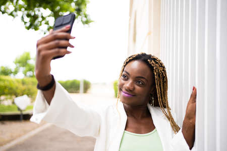 Smiling young african woman taking selfie with a mobile outdoorsの写真素材