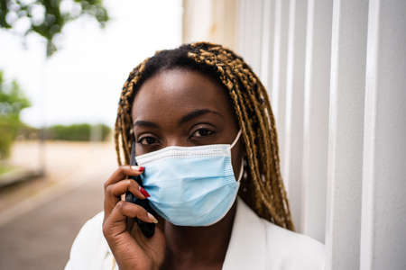 portrait of an african woman with facial mask talking to the mobileの写真素材