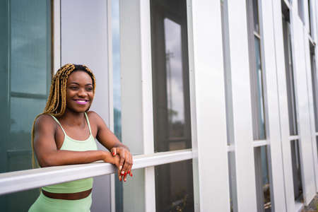 Smiling sportive african woman leaning on the railing of a modern buildingの写真素材