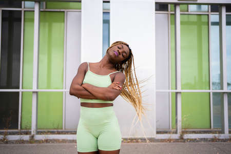 Strong afro woman in sports clothes waving her hair in front of an urban facadeの写真素材