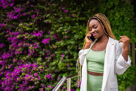 Sportive african woman standing while talking on the mobile next to a gardenの写真素材