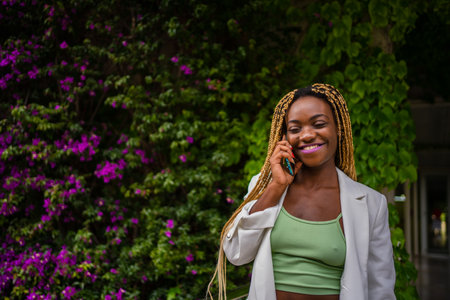 African woman in sports clothes talking on the mobile next to a gardenの写真素材